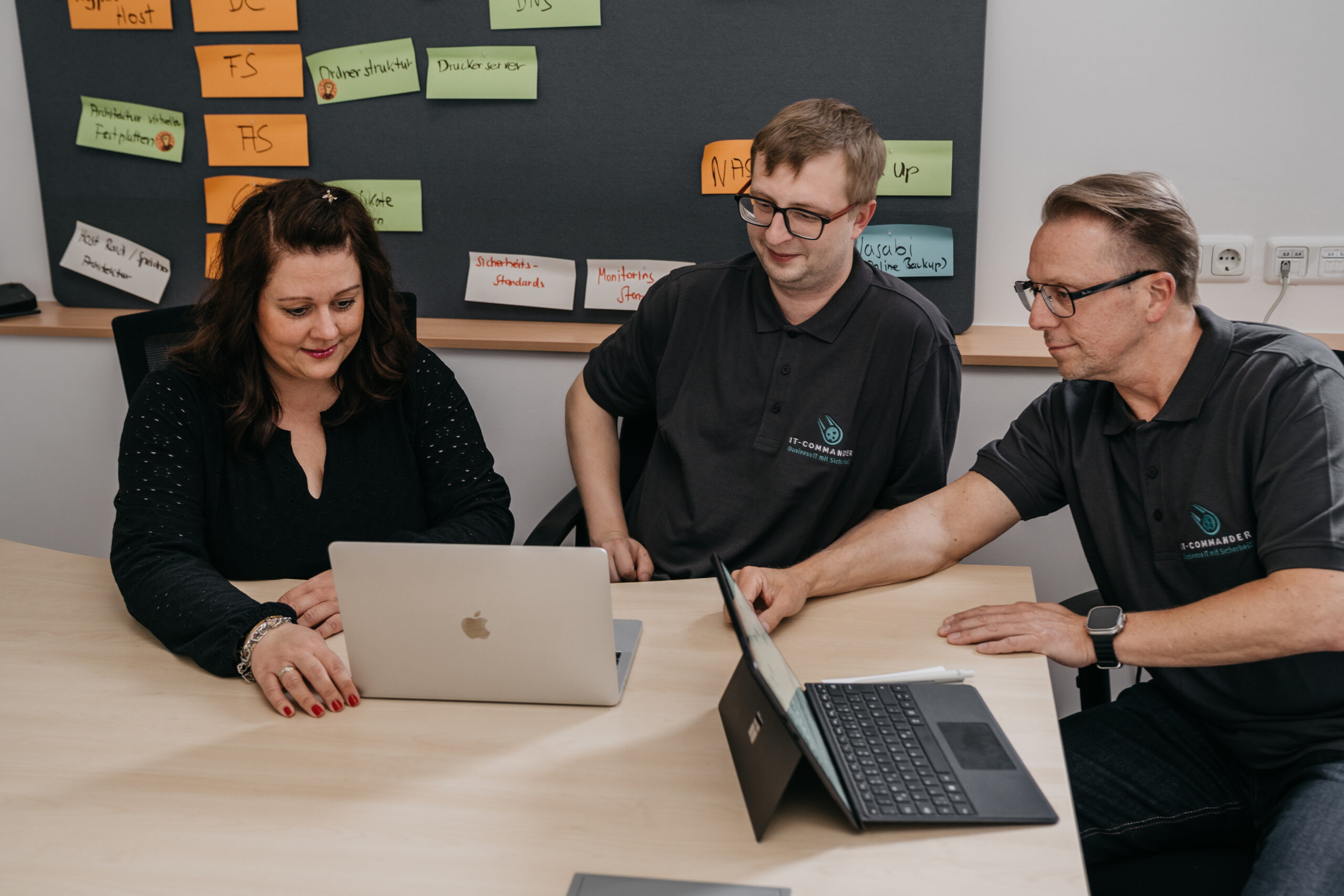 Drei Personen in einem Besprechungsraum arbeiten an Laptops und diskutieren über Inhalte auf einem Tisch.