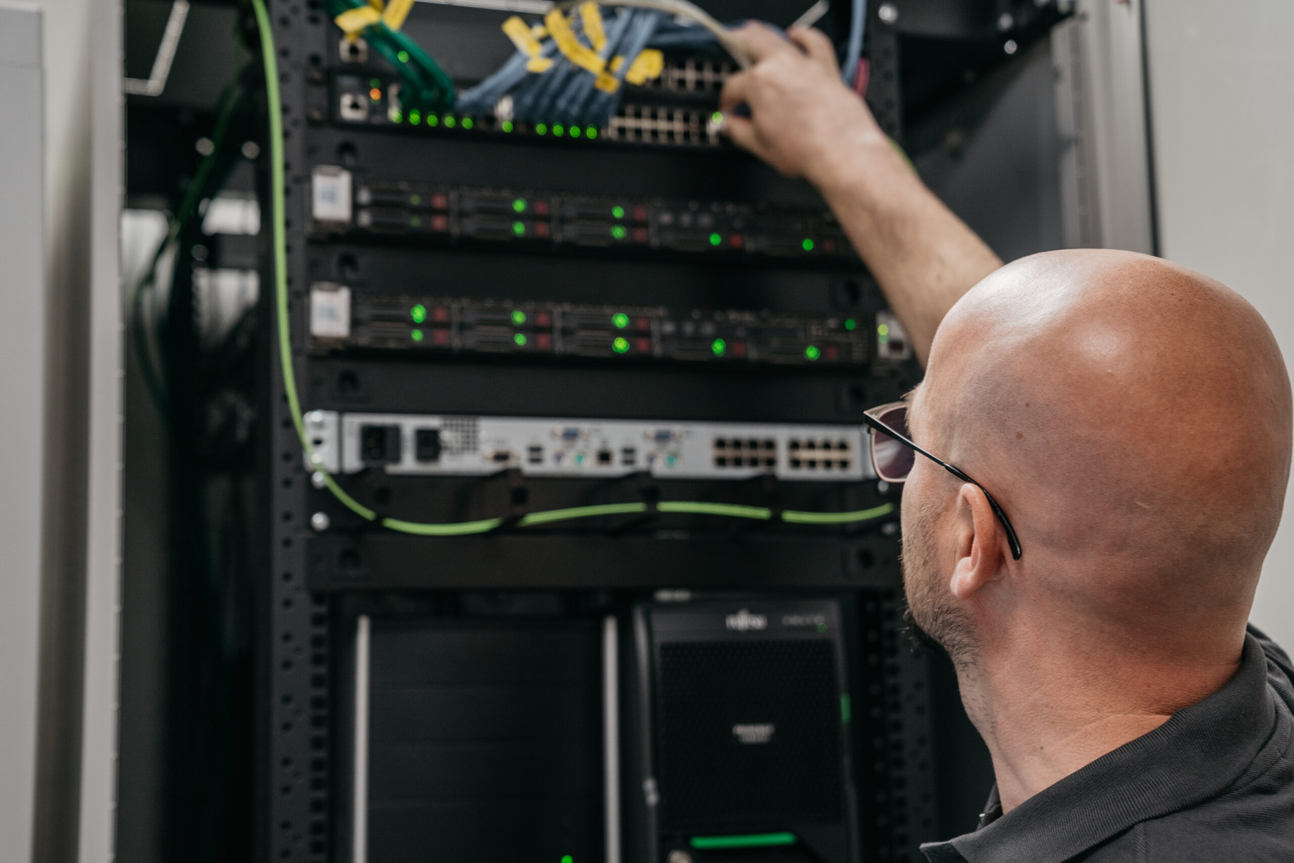 Techniker arbeitet an einem Server-Rack mit leuchtenden Netzwerkgeräten und Kabeln.